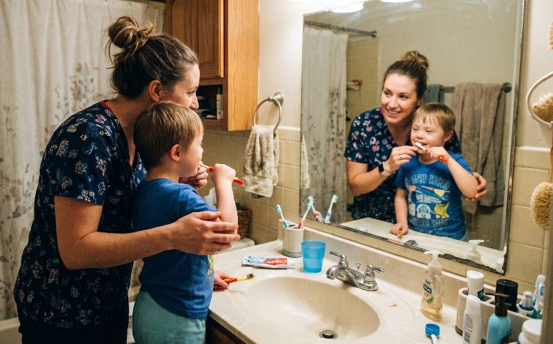 A specialist coaching a child through brushing teeth at the bathroom sink.